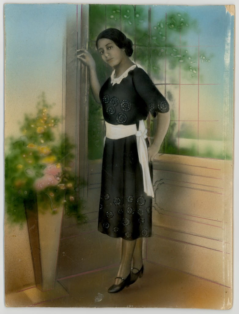Hand-colored portrait of a woman standing in a domestic interior
