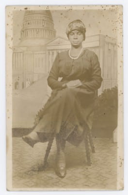 Studio portrait of an unidentified seated woman in front of Capitol Building backdrop