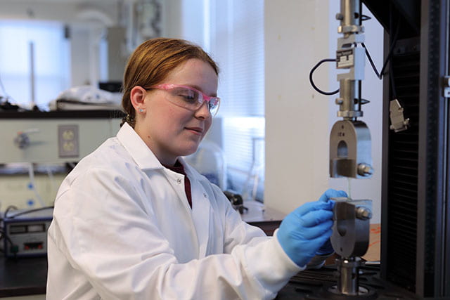 undergraduate student in white lab coat sets up a test on scientific equipment