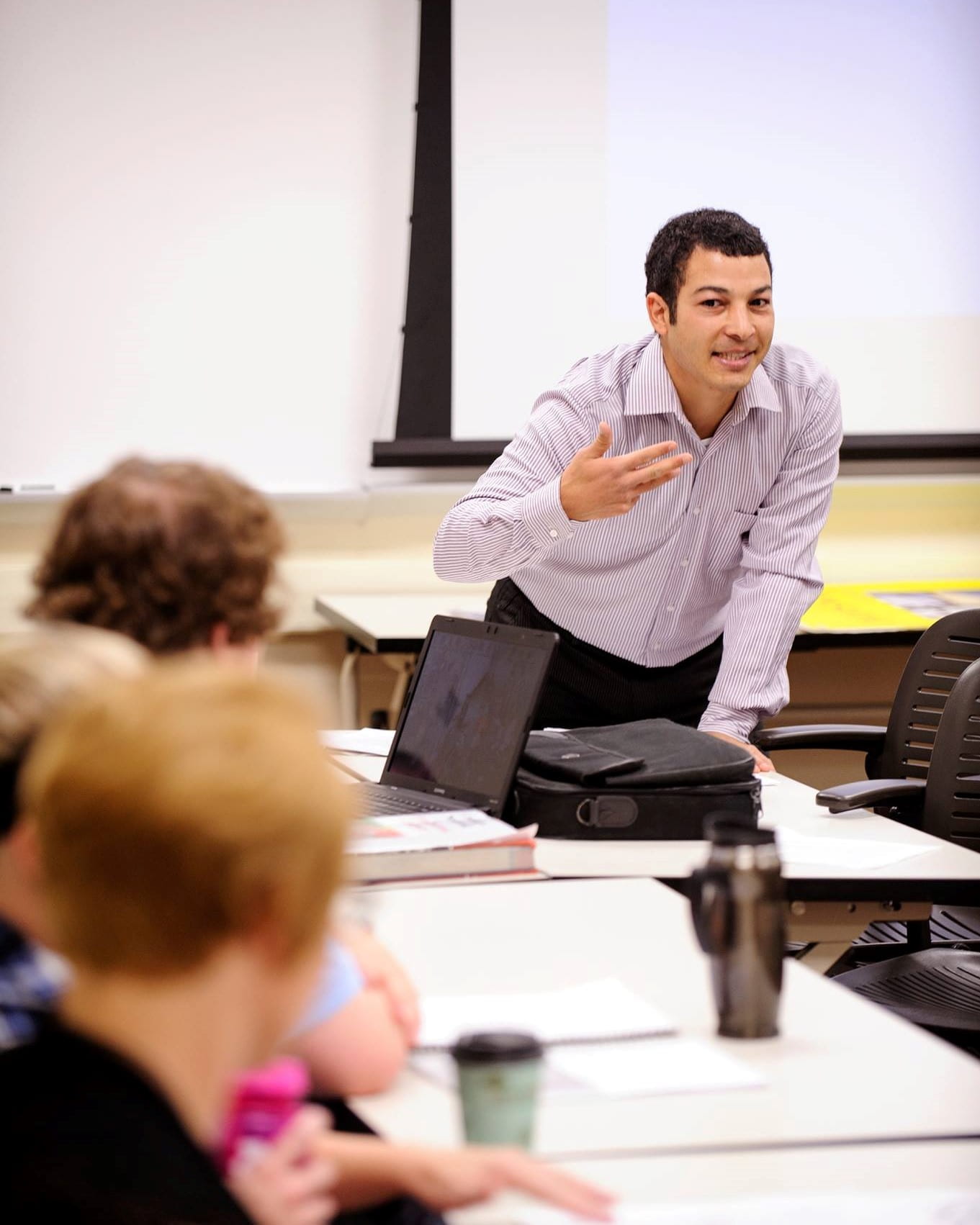 This photo shows Assistant Professor Adil Bentahar standing at the front of the classroom and gesturing to three students.