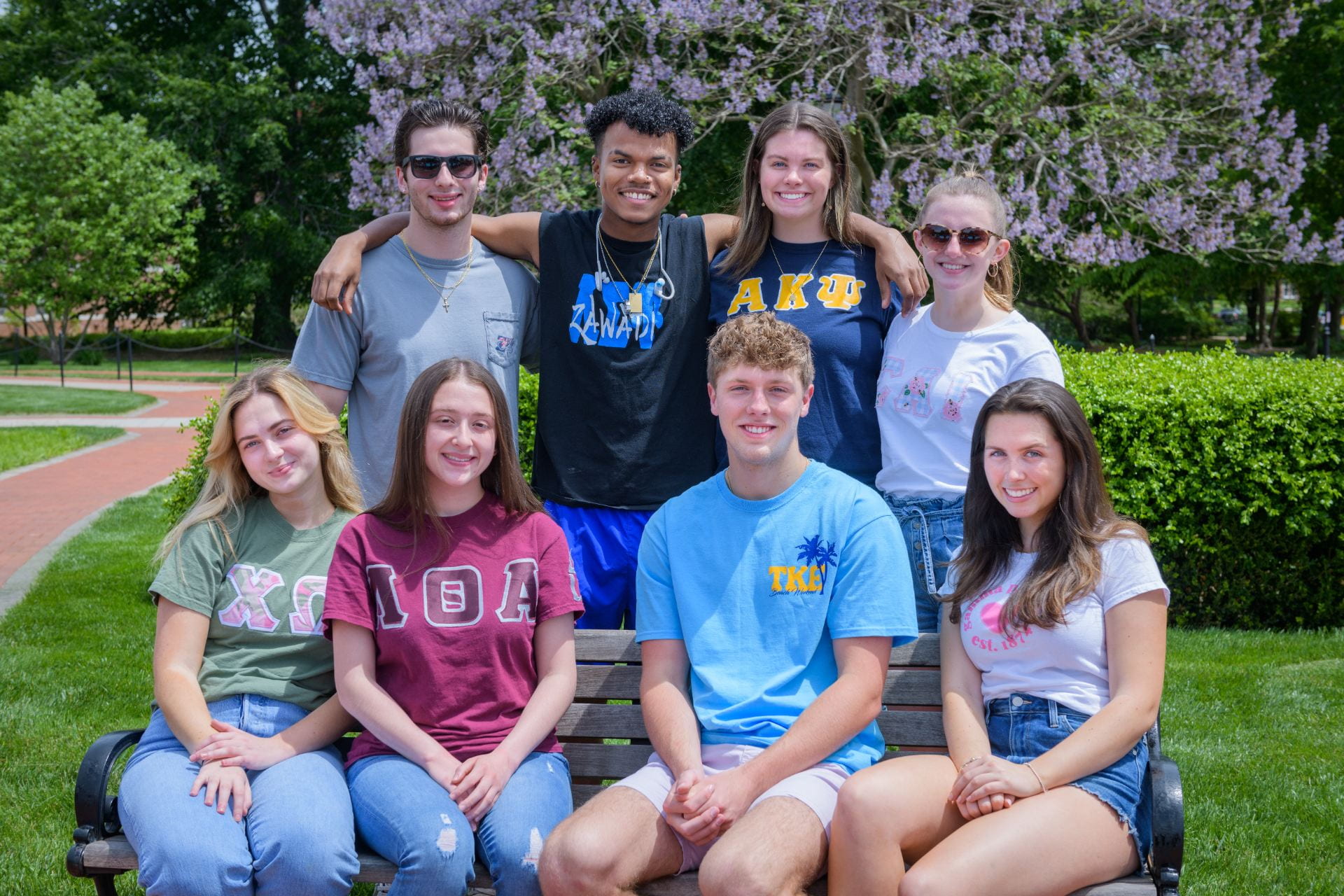 Students wearing fraternity and sorority letter shirts pose for a group photo
