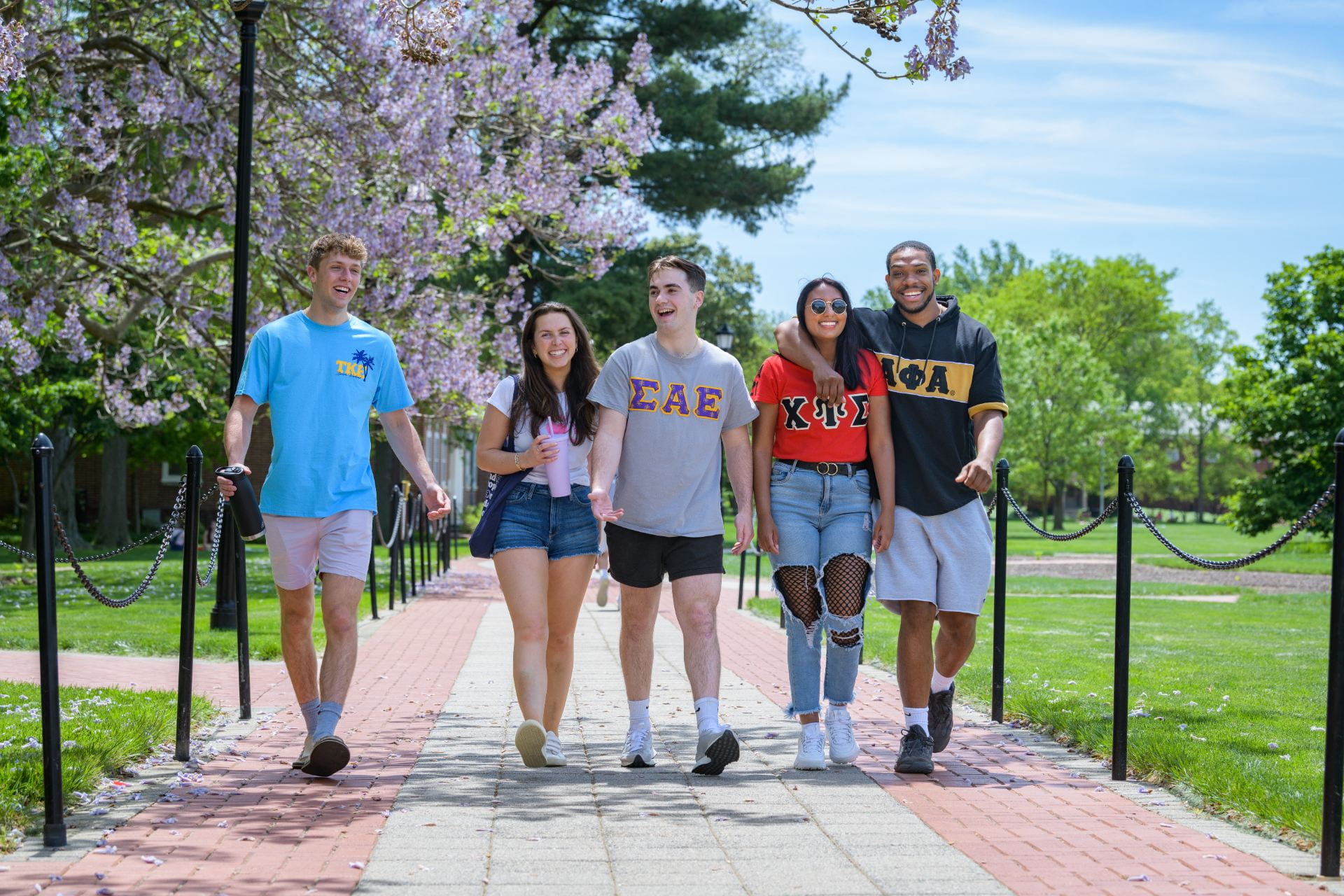 Students in fraternity and sorority letter t-shirts walking and smiling on a sunny day