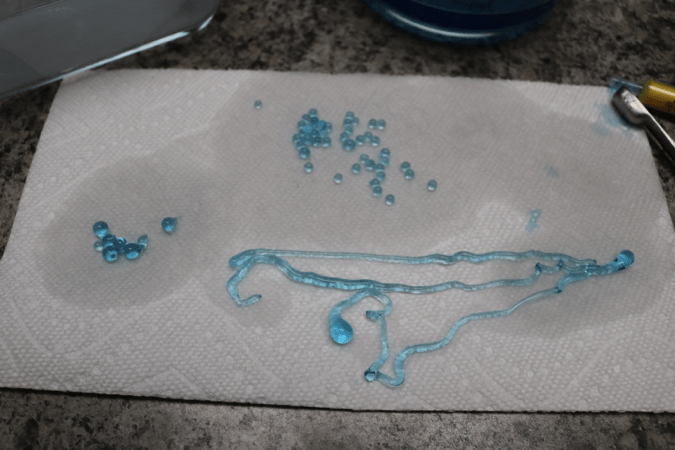 A photograph of a paper towel, with blue boba balls of various sizes and shapes on it, including sphere, teardrop, and long squiggly worm shapes.