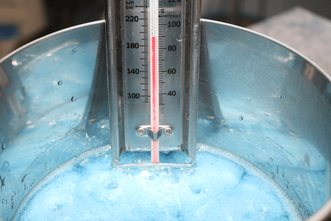 A picture of a saucepan with sodium alginate and distilled water solution bubbling, with a thermometer indicating the temperature at 190˚F.]