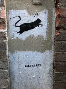A black rat stenciled over white painted background on a building. The words “BLECK LE RAT” appear stenciled below.