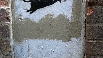 A black rat stenciled over white painted background on a building. The words “BLECK LE RAT” appear stenciled below.