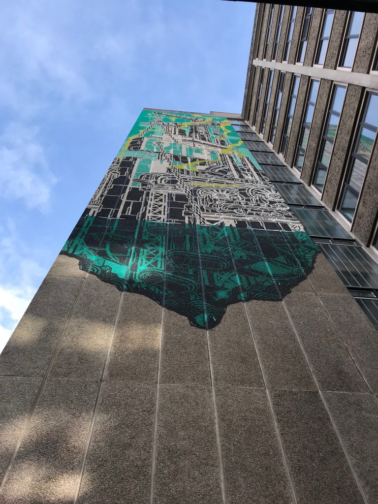 Two images showing a graphic on a building of cranes in the process of constructing a building. The stencil work is turquoise, lime green, black, and white.