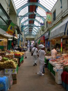 Interior view of market stalls in Brixton Village. Fresh seafood and meat market stalls (right) face the plantains and other produce (left).