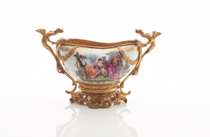 Photograph of Meissen Porcelain Bourdaloue with intricate painted floral decoration and gold dragon mounts. The dragon mounts and gold stand securely hold the porcelain bourdaloue.