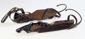 Pair of early nineteenth century ice skates from the Winterthur Collection. The skates consist of a flat, wood bottom with black leather straps to hold the wooden bottom onto the foot and an iron blade which extends far beyond the boot and terminates in an upward curve over the toe.