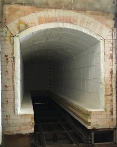 A modern kiln, clean and painted white on the inside. Metal tracks stretch inside of the kiln on which shelves of pottery are slid in to be fired.