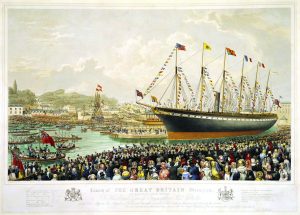 A large steamship decked in nautical and national flags sits in a harbor while a sea of onlookers dressed in colorful bonnets and top hats looks on.
