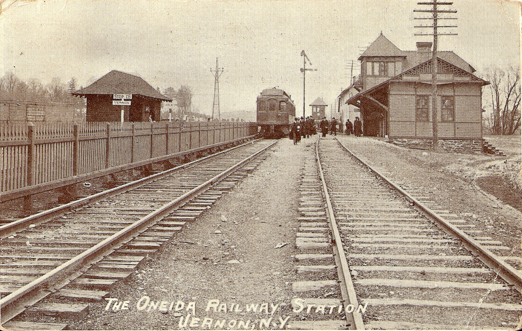 Photo of Oneida Rail Station – a late nineteenth century crowd gathers around a train, ready to board.