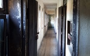 A view down a long, narrow corridor shows the bare plaster walls of a slave dwelling.  The walls are covered in chipped white paint.  At the end of the corridor is a wall covered in chipped mint-green paint.