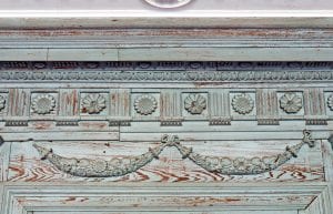 A close-up view shows an intricately carved wooden crown molding with heavily worn blue-green paint.
