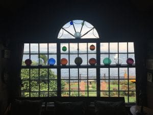 A window, through which a garden and harbor can be seen. Displayed in the window are multicolored glass orbs intended to catch the light.
