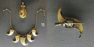 A round, gold pendant with a central tiger claw, a gold chain necklace with five dangling tiger claw pendants hanging down, a brooch made of two tiger claws banded with a gray metal adorned with a sculpted piece of metal shaped like a musket.