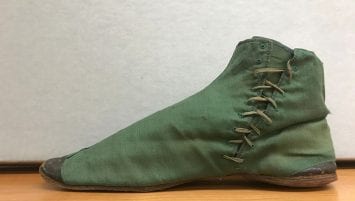 The right shoe of a pair of green ladies’ half boots, rising to the ankle with green shoe laces up the inside of the shoe. Black leather shoe toe and heel.