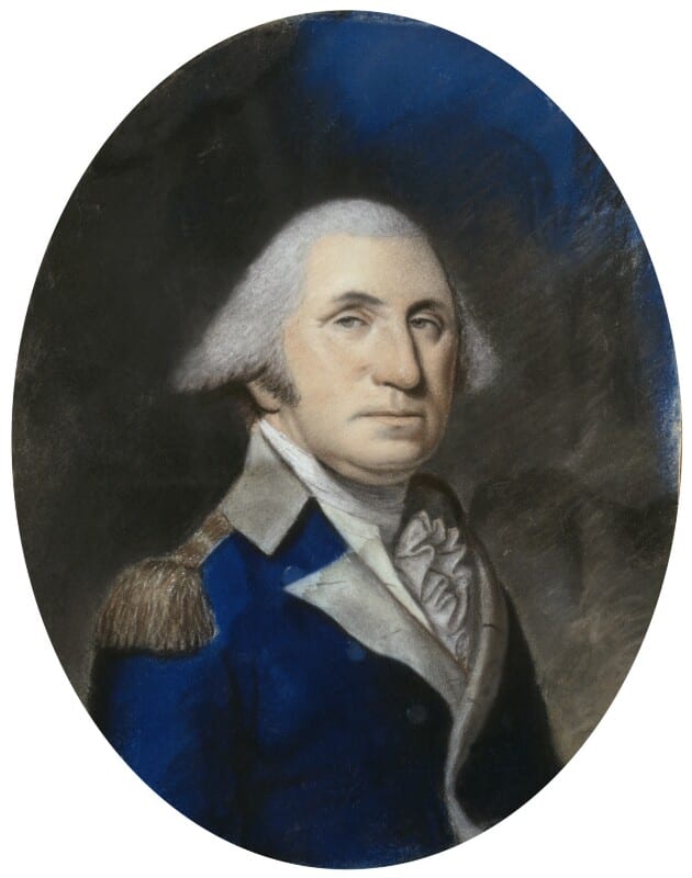  A man with white hair wearing a blue coat sits in three-quarter view against a gray background.