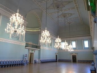 Five huge chandeliers hang in a large blue ballroom with extensive decoration on the ceiling.