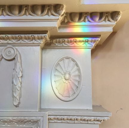 A fireplace molding with rainbow light refracted through a chandelier prism.