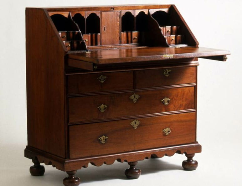 A slant-front desk with an open lid and chest of drawers beneath on five round feet.