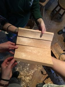 Five hands support four curved wooden planks to demonstrate how they could fit together to make a bucket.
