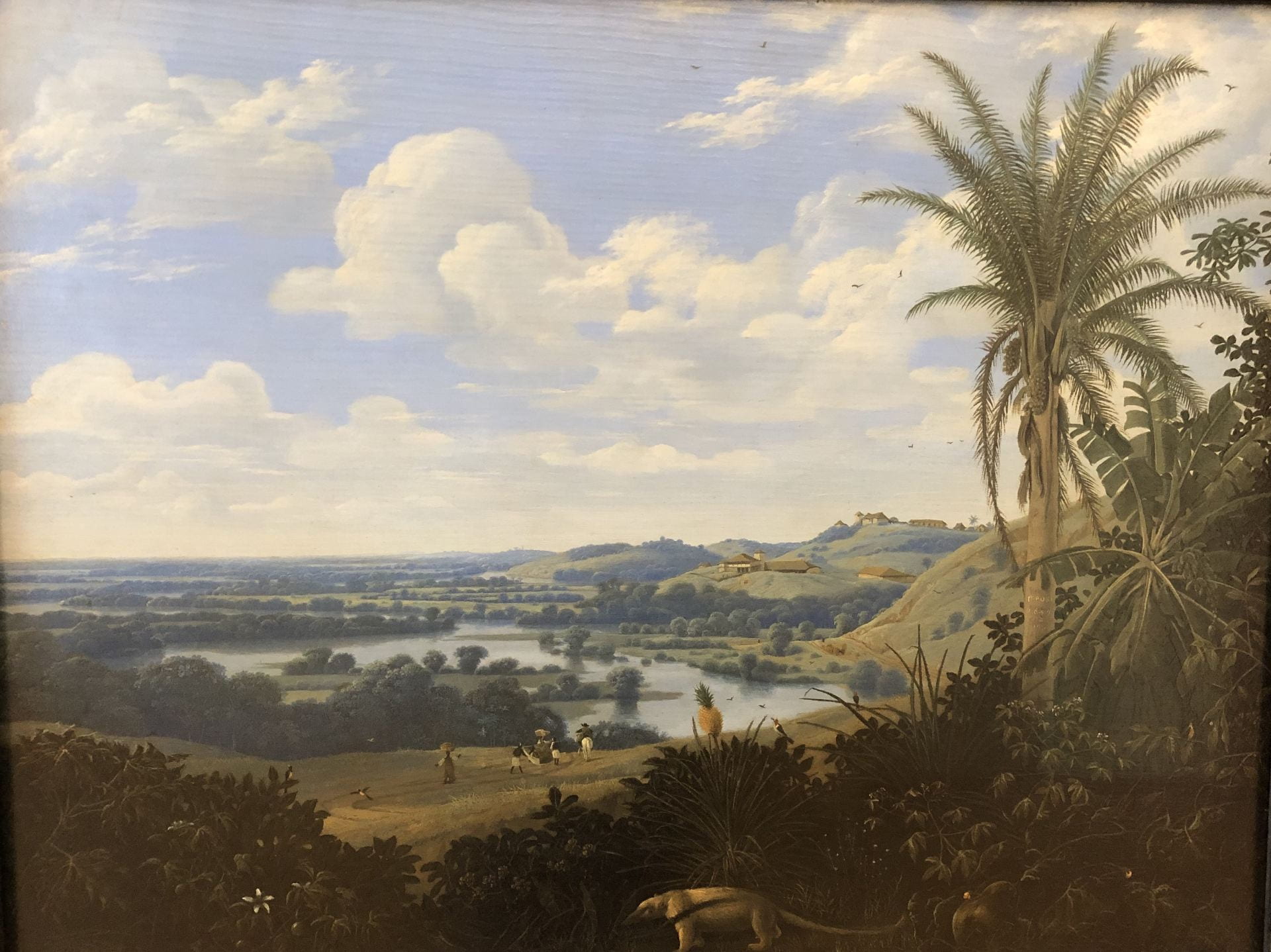 A landscape with large palm tree at right. An anteater walks through the foreground. The middle- and back-grounds are dominated by bands of golden pasture and darker forest, all below a large blue sky. 