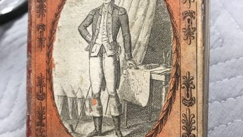 Glass flask covered with orange paper featuring a print of George Washington, the title “Washington,” and a poem in French.