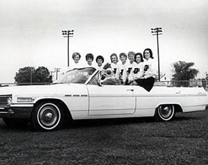 Photograph of cheerleaders and Blue Hen mascot in a car at homecoming. Undated.