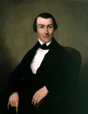 19th century portrait painted on a grayish green background and a white man centered with a suit on. He is looking directly back at the viewer and has a neutral facial expression. Hands are visible near the bottom of the image on top of black suit.