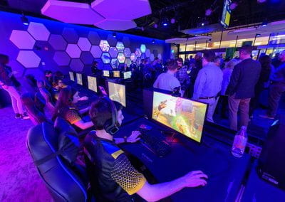 Students play at a row of video game stations as guests gather in the Esports Arena