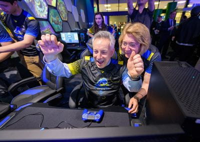 President Assanis cheers as he tries a video game while First Lady Assanis watches over his shoulder