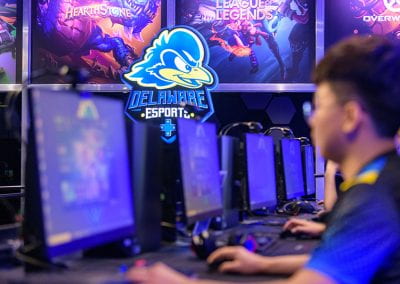 Delaware Esports lit sign with student playing at gaming station in foreground