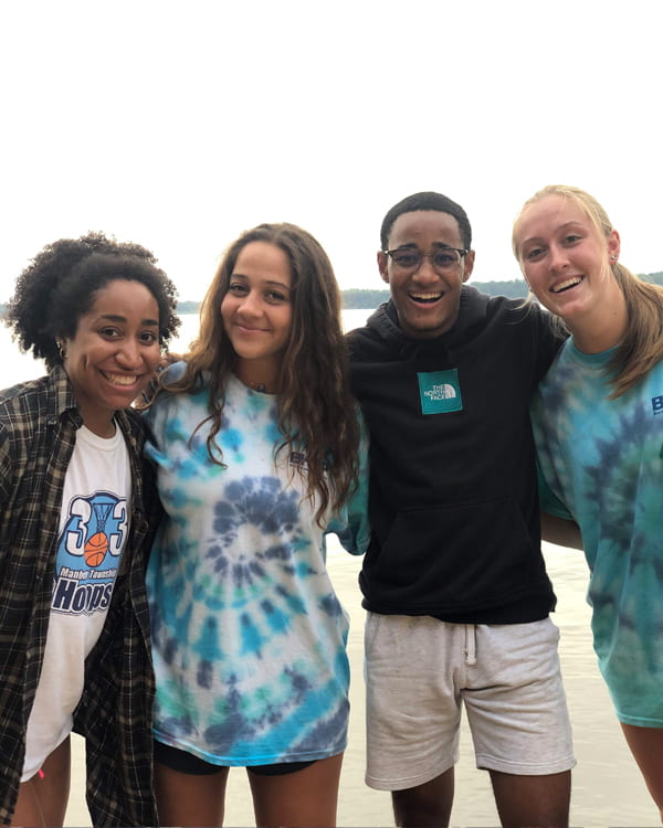 4 students pose by the water at a service project