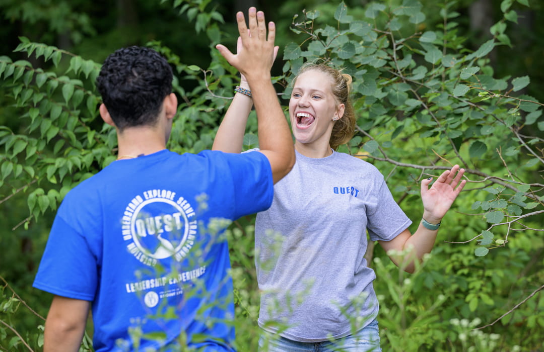 two students high-five amid foliage at a service event